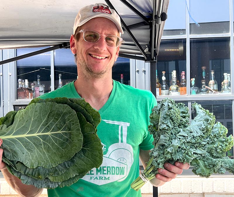 A smiling man holds up hands full of kale and greens