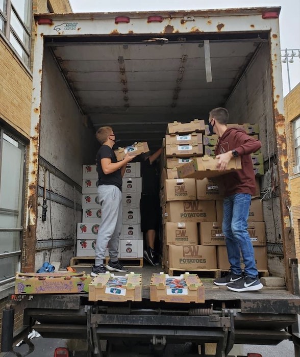 Two teens load boxes of food into a large truck