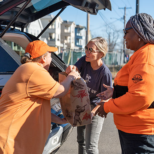 A Food Rescue US volunteer hands a bag of food to 2 women at a receiving agency