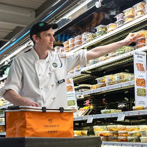 A grocery store employee places food from a shelf into a Food Rescue US bag