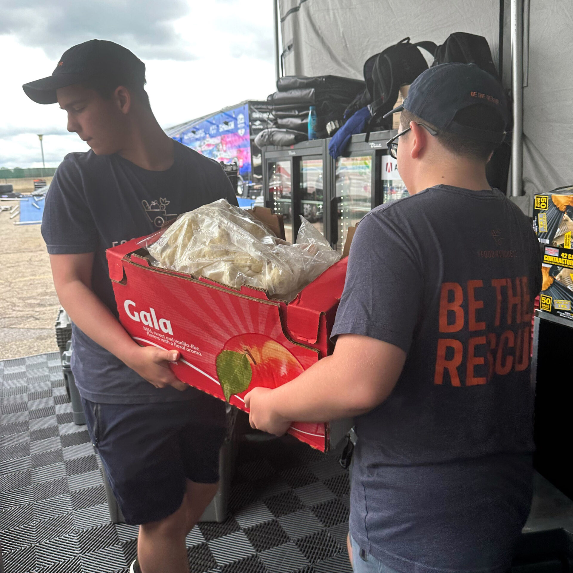 Two volunteers carry a large box of food donations from the Detroit Grand Prix