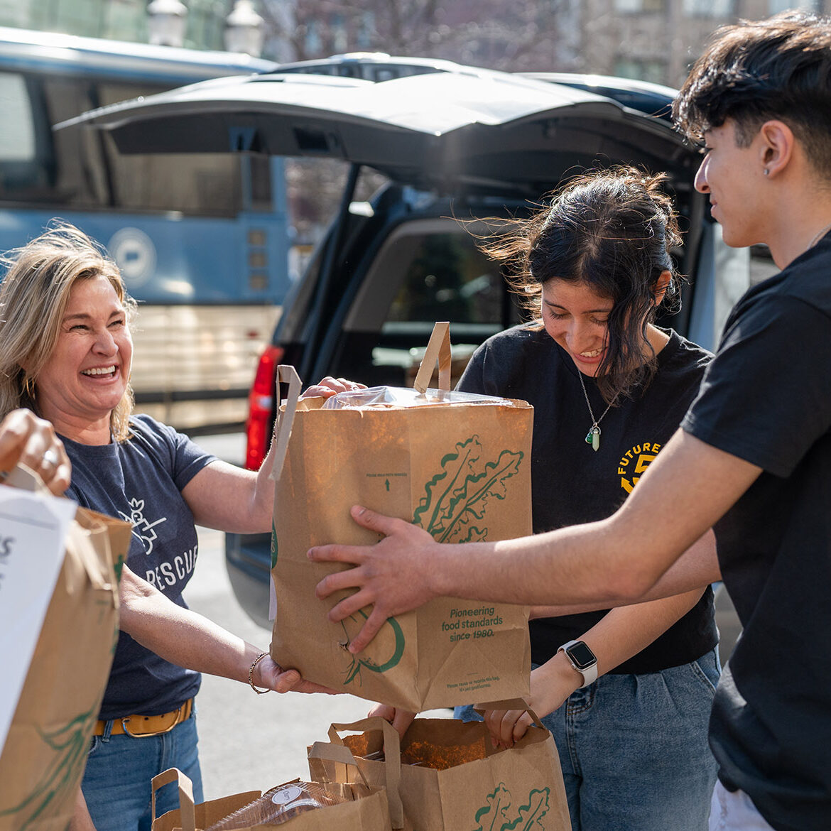 A woman hands a bag of food to young volunteers