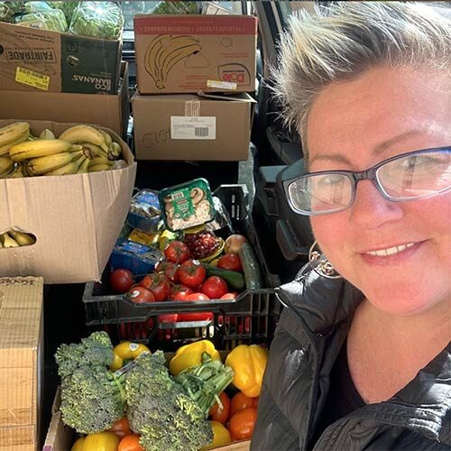 A Food Rescue US volunteer smiles in front of boxes full of fruits and vegetables