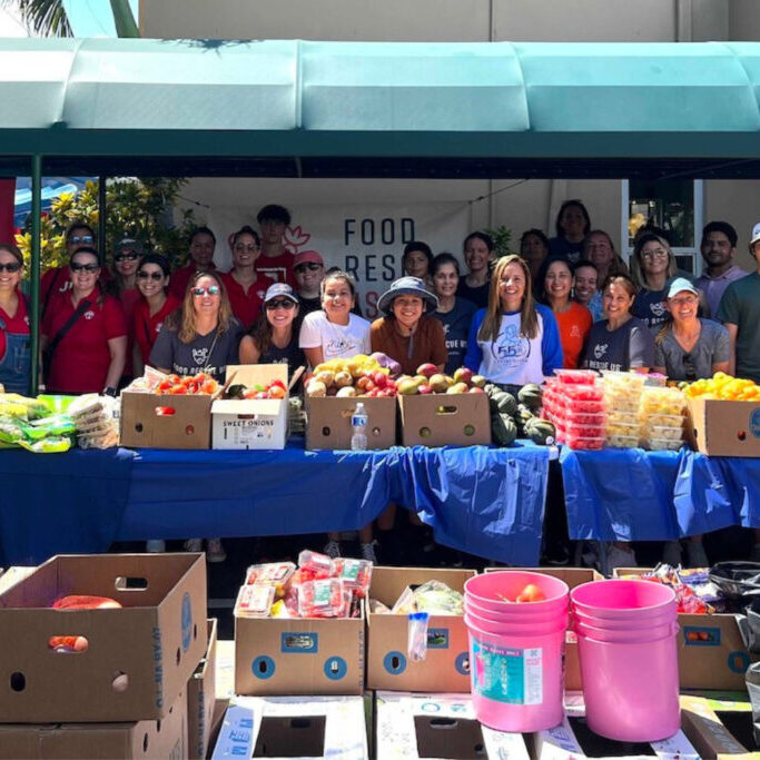 A large group of volunteers poses with tables full of rescued food