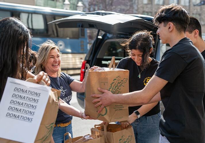 A smiling woman hands bags of food to teen volunteers