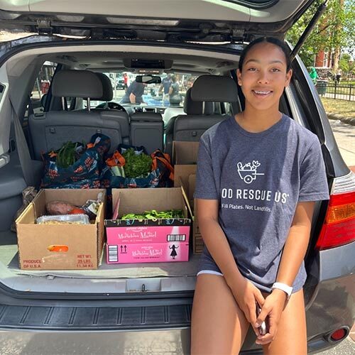 A teen Food Rescue US smiles with a trunk full of rescued food