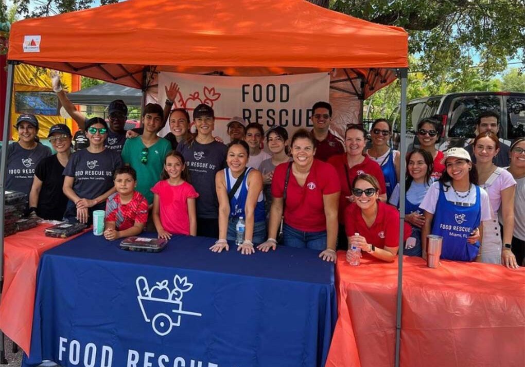 A large and diverse group of people standing at a Food Rescue US table outside in south Florida